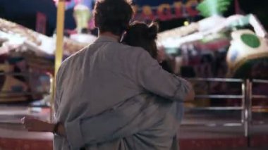 Sevgi dolu çift ayakta ve Eğlence Fuarı'nda aydınlık cazibe bakarak. Parlama ışık, gece