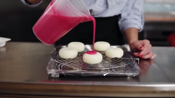 Closeup slow motion shot of a colorful pink mirror glaze being poured on the frosted desserts lying on tray on a metal grid — Stock Video