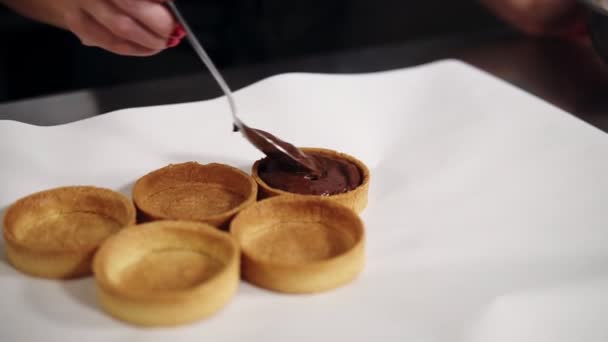 Nahaufnahme von Prozess Füllung gebackene Torten mit Schokoladencreme mit einem Löffel. Arbeitstisch mit weißem Papier bedeckt — Stockvideo