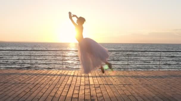 Belle ballerine en tutu blanc dansant, sautant sur le plancher de bois près de la mer ou de l'océan. Soleil brille sur le fond — Video