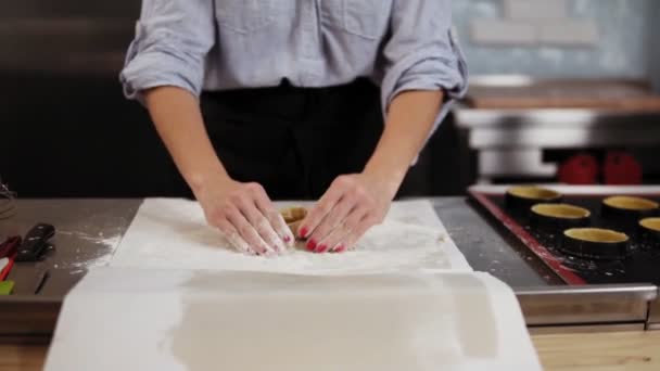 Een mooie Kaukasische blonde banketbakker kneedt gebak deeg op een plateau. Glimlacht, shakes uit meel uit handen klappen. Vooraanzicht, slow-motion — Stockvideo