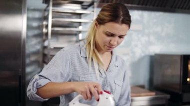 Bir mavi gömlek ve siyah önlük bir pudra krem bir duruma bir mikser kullanarak çelik bir kasede yumurta akı kaIktı