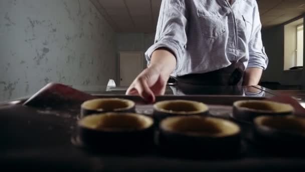 Une femme pâtissière sort des parcelles cuites au four pour le dessert, tartelettes. Cuisine moderne, classe de maître culinaire. Intérieur depuis la vue sur le four — Video