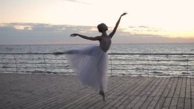 Balerin beyaz Bale tutu ve pointe gündoğumu veya günbatımı okyanus ya da deniz üstünde dolgu üzerinde dans ediyor. Pratik bale pas, performans genç çekici kadın. Ağır çekim