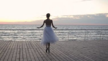 Balerin beyaz tutu ve pointe setin okyanus ya da deniz plaj yukarıda güneş doğarken dans. Klasik çalışmaları duygular ile pratik genç güzel kadın