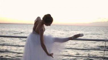 Beyaz tutu ve pointe setin günbatımı okyanus ya da deniz kumsalda yukarıda üzerinde dans eden bir balerin güzel sahne. Şehvetli kadın pratik germe ve klasik egzersizleri yapıyor çubuk üzerinde eğilir.