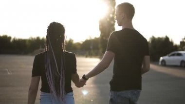Siyah T-shirt ve bir kız tarafından otopark yürüyüş dreadlocks ile siyah gömlekli bir adam. İki aşık. Güneş parlıyor ve arka plan üzerinde