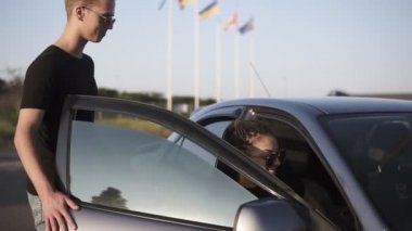 Genç bir insan - erkek ve kadın beklemeliler arabaya. Adam kız arkadaşı için açık araba kapı ve karanlık bir gümüş otomobil sürücü koltuğu için gidin. Gündüz