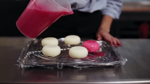 Primo piano filmato, la pasticceria femminile versando smalto specchio rosa su biscotti bianchi preparati su una pentola. Vista frontale — Video Stock