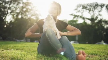 Köpeği ile çimlerde oturan genç güzel kız. Evde beslenen hayvan doğaya açık ile oynarken şirin erkek. Hugs ve öper. Güneş parlıyor ve arka plan üzerinde