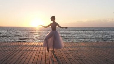 Kadın Bale dansçısı eğitim açık denize yakın bir ahşap dolgu üzerinde havada. Kız beyaz bir tutu giyinmiş. Güneş parlıyor ve arka plan üzerinde