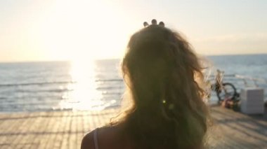 Tanınmayan kız güneşli bir günde yürüyüş arka görünümü. Genç kadın uzun saçlı tatil sırasında hayattan zevk. Arka plan, deniz manzara. Yaz güneşi