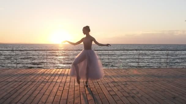 Kobieta balet tancerz szkolenia na zewnątrz na drewniane nasyp w pobliżu morza. Dziewczyna ubrana w biały tutu. Słońce świeci na tle — Wideo stockowe