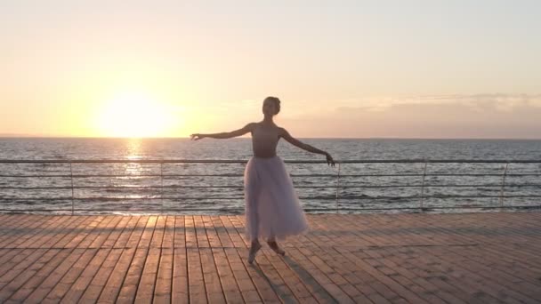 Prachtige slow motion scene van jonge ballerina wervelende op een houten vloer buiten in slow motion. Zee, zon schijnt op de achtergrond — Stockvideo