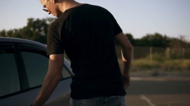 Siyah T shirt ve güneş gözlüğü genç çekici adam Park yerinden kız arkadaşı ile gitmek araba, koyu gümüş renkli sedan ve hazır olsun