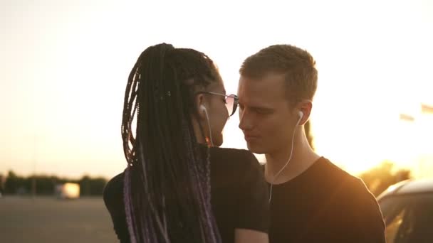 Casal jovem e atraente ouvindo música junto com fones de ouvido brancos. Lá fora na rua, a dançar, a beijar. Casal amoroso a sair juntos. Vista de perto — Vídeo de Stock