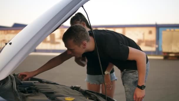 Jonge mensen op een roadtrip die problemen met hun auto, kijken voor de mislukking met motor onder de motorkap. Winkelcentrum parkeren — Stockvideo
