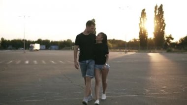 Otopark ve el ele tutuşarak dükkânının önünden yürüyen genç bir şık çift portresi. Mutlu, sevgi dolu bir çift açık havada. Hem denim gömlek ve siyah T shirt giyen. Akşam, günbatımı