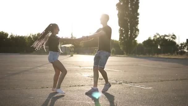 Attractive couple holding by hands and whirling on the parking at leisure. Happy lifestyle, spinning around together. Sun shines on the background — Stock Video