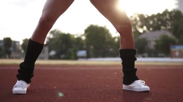 Εξαιρετικά στενή επάνω πλάνα από γυμνασμένα πόδια από μια αθλήτρια που κάνει σταυρό πόδια άλματα και καταλήψεις. Κοπέλα φορώντας κάλτσες μαύρο γκολφ και λευκά αθλητικά παπούτσια. Αργή κίνηση — Αρχείο Βίντεο