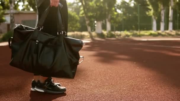 Close up van de voeten in het zwarte sneakers-fit jonge vrouw naar het stadion met de bruine bekleding gaat. Er is een zwarte sport zak in haar hand en ze zet het op de grond — Stockvideo