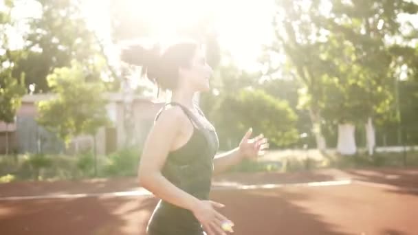 Ταιριάζει γυναίκα στο μαύρο σπορ σουτιέν και την μπλούζα τρέξιμο σε εξωτερικούς χώρους. Μελαχρινή κοπέλα με το τρέξιμο happilly ουρά πόνι. Ηλιακό φως — Αρχείο Βίντεο