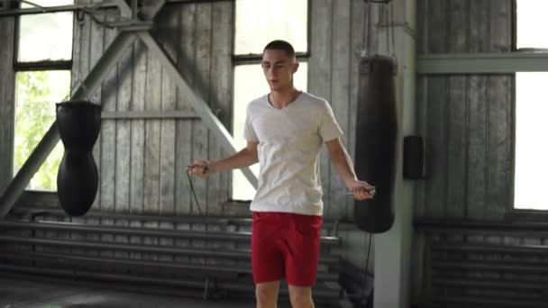 Imágenes en cámara lenta de un atleta caucásico de pelo corto haciendo ejercicio en el gimnasio de boxeo. Saltar sobre una cuerda. Deporte, boxeo, trabajo duro concepto — Vídeos de Stock