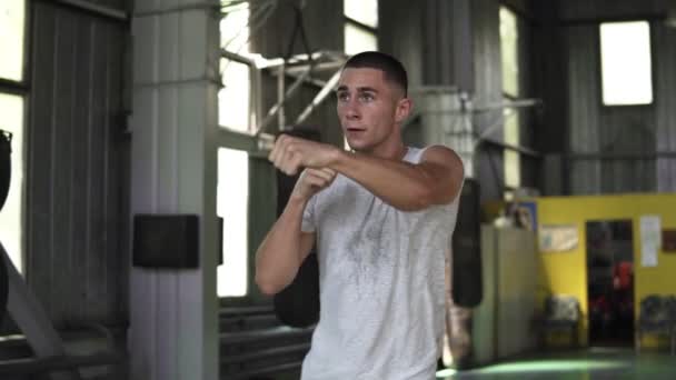 Медленная съемка сильного молодого человека в футболках, боксе и ударах невидимым противником во время тренировки в спортзале. Спорт, бокс, фитнес концепция — стоковое видео