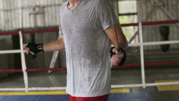 Jovem boxeador com as mãos enroladas em bandagem pulando na corda em um ginásio de boxe. Movimento lento, anel de boxe no fundo — Vídeo de Stock