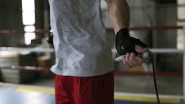 Homem de cabelos curtos, caucasiano em camiseta branca e camisa vermelhatrabalhando duro no ginásio de boxe. Exercício ligeiro com corda de salto. Imagens direcionadas de mãos em bandagem — Vídeo de Stock