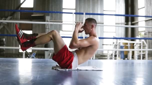 A man is exercising in the gym. Lying on the back and lifts up his chest with legs up, abdominal press exercise. Boxing ring, indoors — Stock Footage A man is exercising in the gym. Lying on the back and lifts up his chest with legs up, abdominal press exercise. Boxing ring, indoors Stock Video