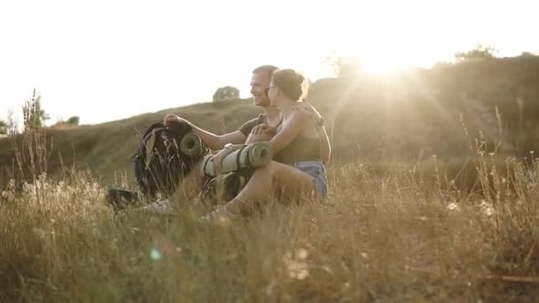 Wandelen paar - wandelaars rustend op een heuvel. Jonge vrouw en man wandelaar zittend op de grond genieten van uitzicht gelukkig, glimlachen knuffelen. Jong koppel wandelen, ontspannen na een wandeling — Stockvideo