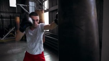 Beyaz erkek boxer T gömlek ve kırmızı gömlek spor salonunda çalışma dışarı. Pratik başladı ve kum torbası ile puches. Studio iç boks