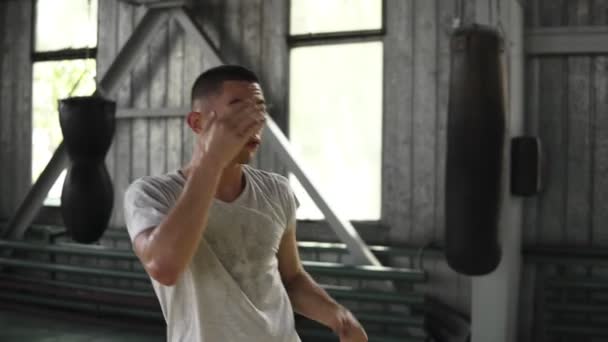 O jovem boxeador treina. O cara executa chutes por um oponente invisível, foge, imitando boxe. Aquecimento no ginásio de boxe — Vídeo de Stock