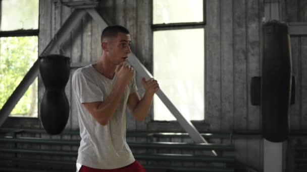 Zijaanzicht van een mannelijke boxer aan het warmrijden in de boksen sportschool. Geconcentreerd op het beoefenen van beroertes, vechten met onzichtbare tegenstander — Stockvideo