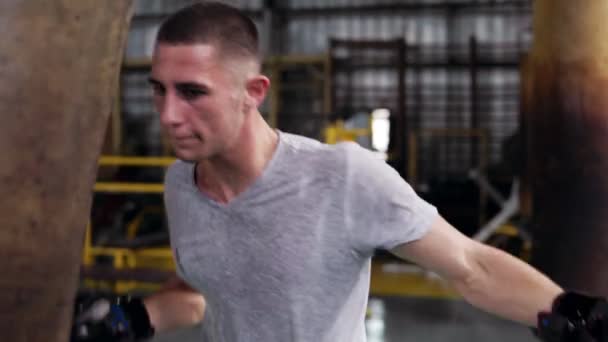 Zbliżenie na młodych, krótkie włosy mężczyzna bokser Dokonywanie silny puches w czarne rękawice bokserskie. Wypracowania z workiem w studio na bokserskich — Wideo stockowe