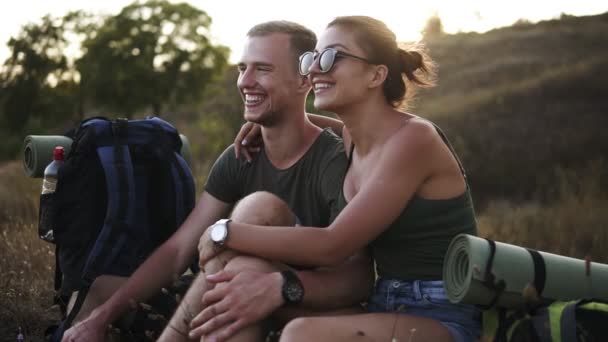 Close up footage of young caucasian couple sitting on mountain or hill ledge looking at each other and talking, embracing, happy, smiling. Resting after trekking — Stock Video