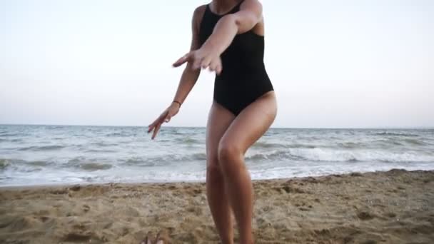 Piękne, brunetka dziewczyna w czarny strój kąpielowy szczęśliwie działa przy plaży, biorąc rękę swojego chłopaka i prowadzące do morza. Uśmiechnięty, zadowolony, patrząc na kamery — Wideo stockowe