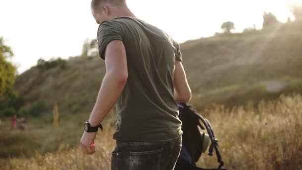 Joven hombre caucásico, viajero sacando su mochila en el suelo y se sienta en la hierba frita para descansar durante el senderismo. Agua potable de la botella de plástico — Vídeo de stock