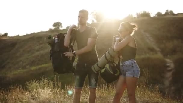 Çift hiking. Onların sırt çantaları yere tespit genç kadın ve erkek uzun yürüyüşe çıkan kimse. Onların birlikte, mutlu, elinde eller gülümseyen vaktinizi git hazır. Genç çift doğa yürüyüşü — Stok video