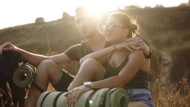 Couple de randonneurs - randonneurs reposant sur une colline. Jeune femme et homme randonneur assis sur le sol jouissant d'une vue souriant heureux, étreignant. Randonnée en couple, détente après la randonnée — Video