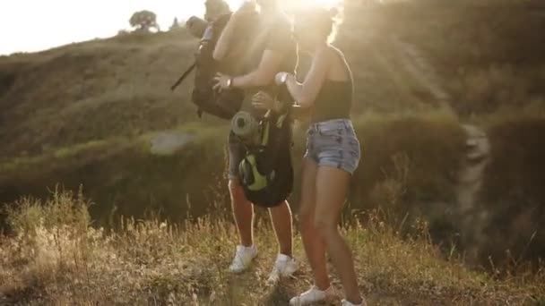 Två vita trevellers tar resten på en kulle under sin vandring. Ta av ryggsäckarna och sitta på marken, dricksvatten från en plastflaska. Närbild bilder — Stockvideo