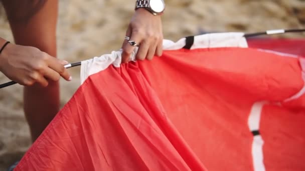 A man and a woman are traveling. Together they set up a red tent on the beach near the sea in windy weather. Close up footage — Stock Video