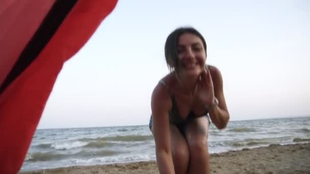 Spåra footage från röda tält av en härlig, brunett flicka i denim kort som ringer för att gå med henne och kör till havet vid stranden — Stockvideo