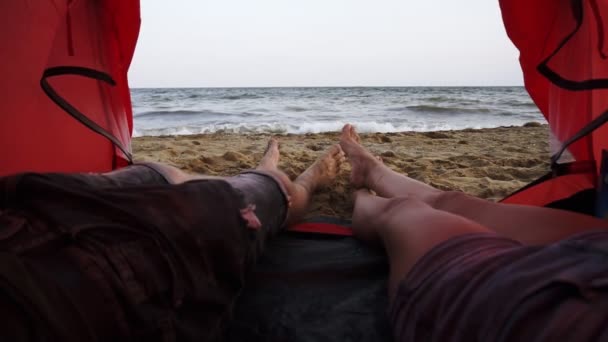 Cena alegre de casal youg relaxado ter um descanso na tenda e olhando para o mar ou oceano. Fechar os pés, imagens de dentro — Vídeo de Stock