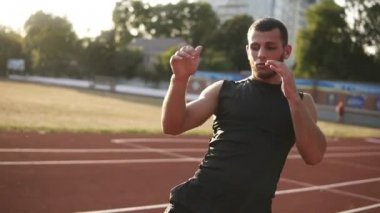 Eğitim için hazırlık bir koşu parkuru Stadyumu, bacaklarını esnetiyor kaslı sporcu genç erkek. Bacaklarını kaldır. Güneş parlıyor