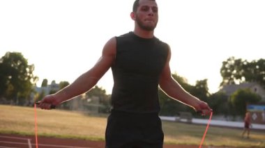 Bir atlet açık havada siyah spor stadyum yolda ip atlama üzerinden atlama Handhelded görüntüleri. Güneş parlıyor ve arka plan üzerinde