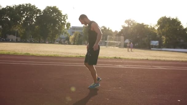 ランニングやトレーニングの準備をしてスタジアムでトラックの彼の手を伸ばす若い選手男性の Handhelded 映像。スポーツと人々 — ストック動画