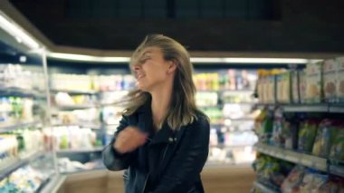 Süpermarkette: siyah ceketli mutlu genç kadın mal ve süt ürünleri ile raflarda dans ediyor. Döne döne, eğleniyor, pozitif