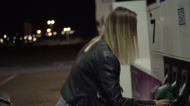 Mujer rubia con chaqueta de cuero saca la pistola de gasolina y cierra el tanque de gasolina. Sonriente chica está lista para continuar su camino — Vídeo de stock